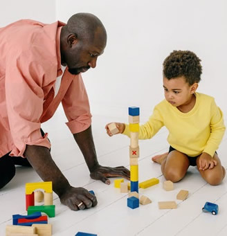 man and young boy sitting on the ground stacking blocks.